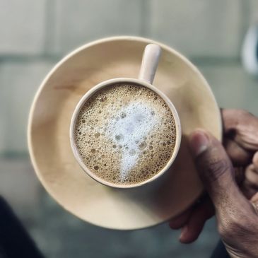 Hand holding a cup of frothy coffee on a matching saucer.