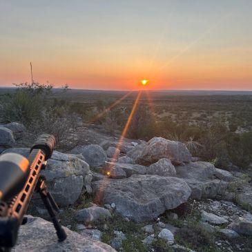 Sunset over rocky terrain with a rifle in foreground.
