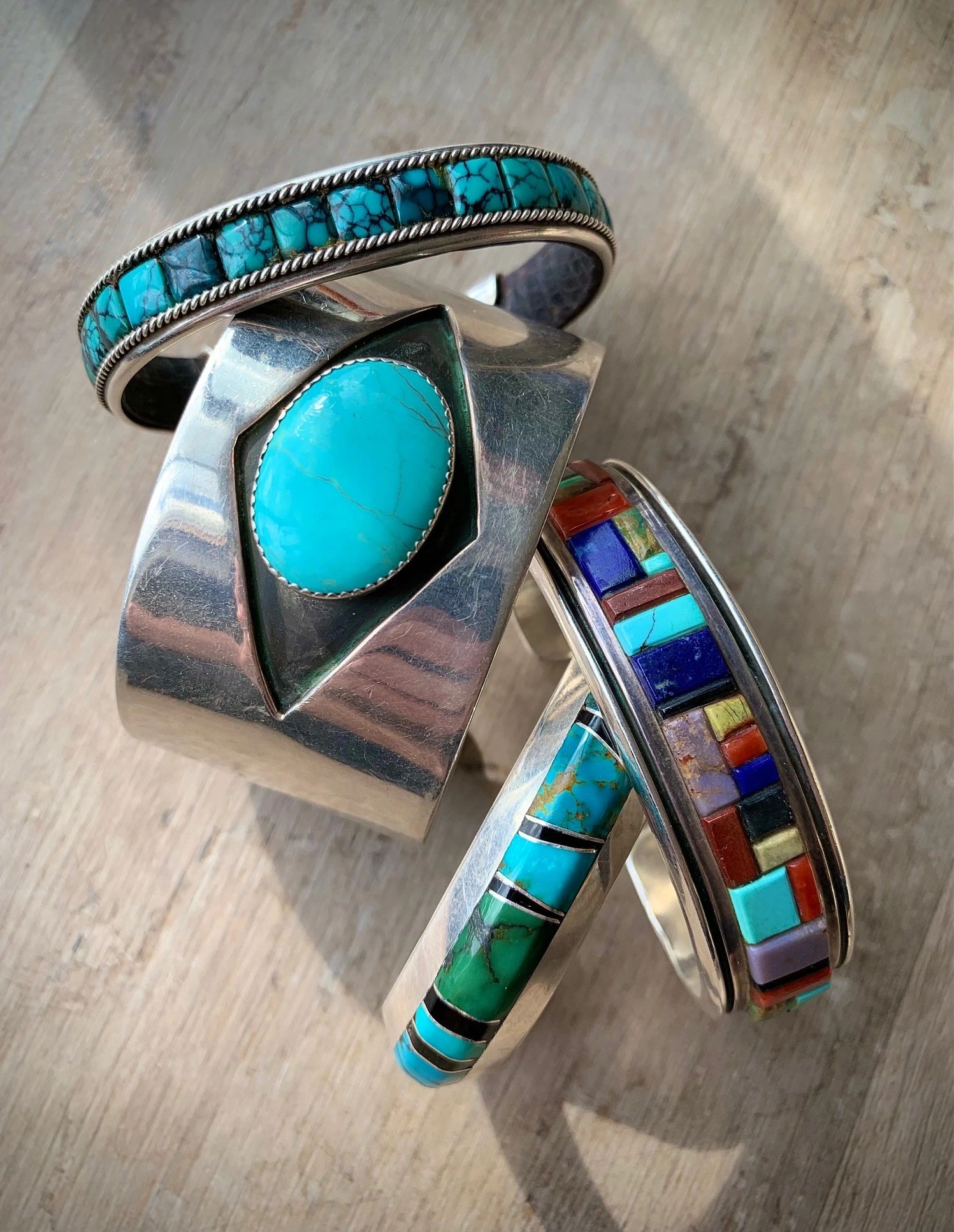 Four silver bracelets with colorful stones on a wooden surface.