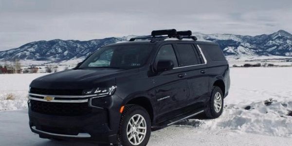 Black Chevy SUV parked on snowy landscape with mountains in the background.
