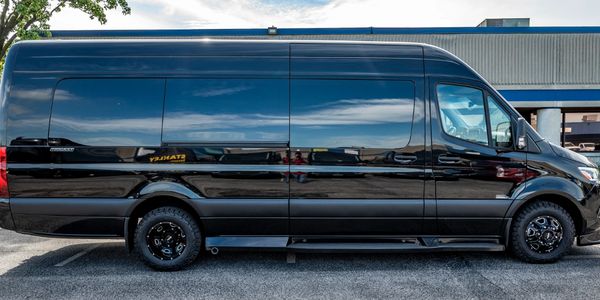 Black luxury van parked outside a building on a sunny day.
