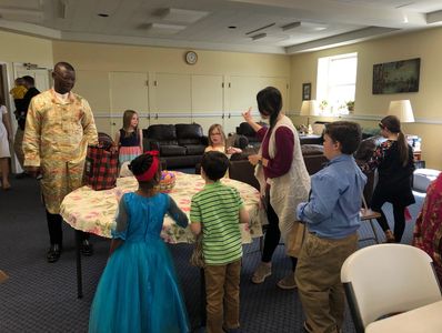 Children and adults gathered around a table in a cozy room, engaging in an activity.