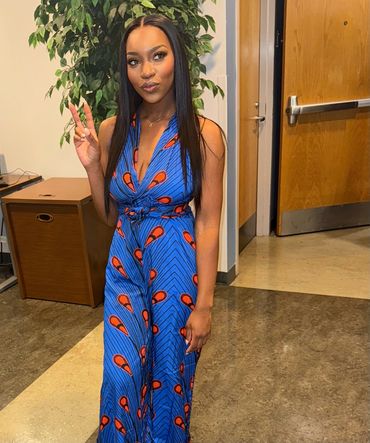 Woman in blue patterned dress making a peace sign indoors.