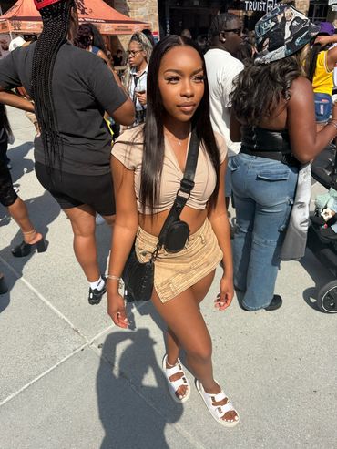 A young woman in a beige crop top and mini skirt at an outdoor event.
