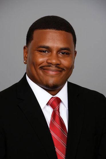 Smiling man in a black suit and red striped tie against a gray background.