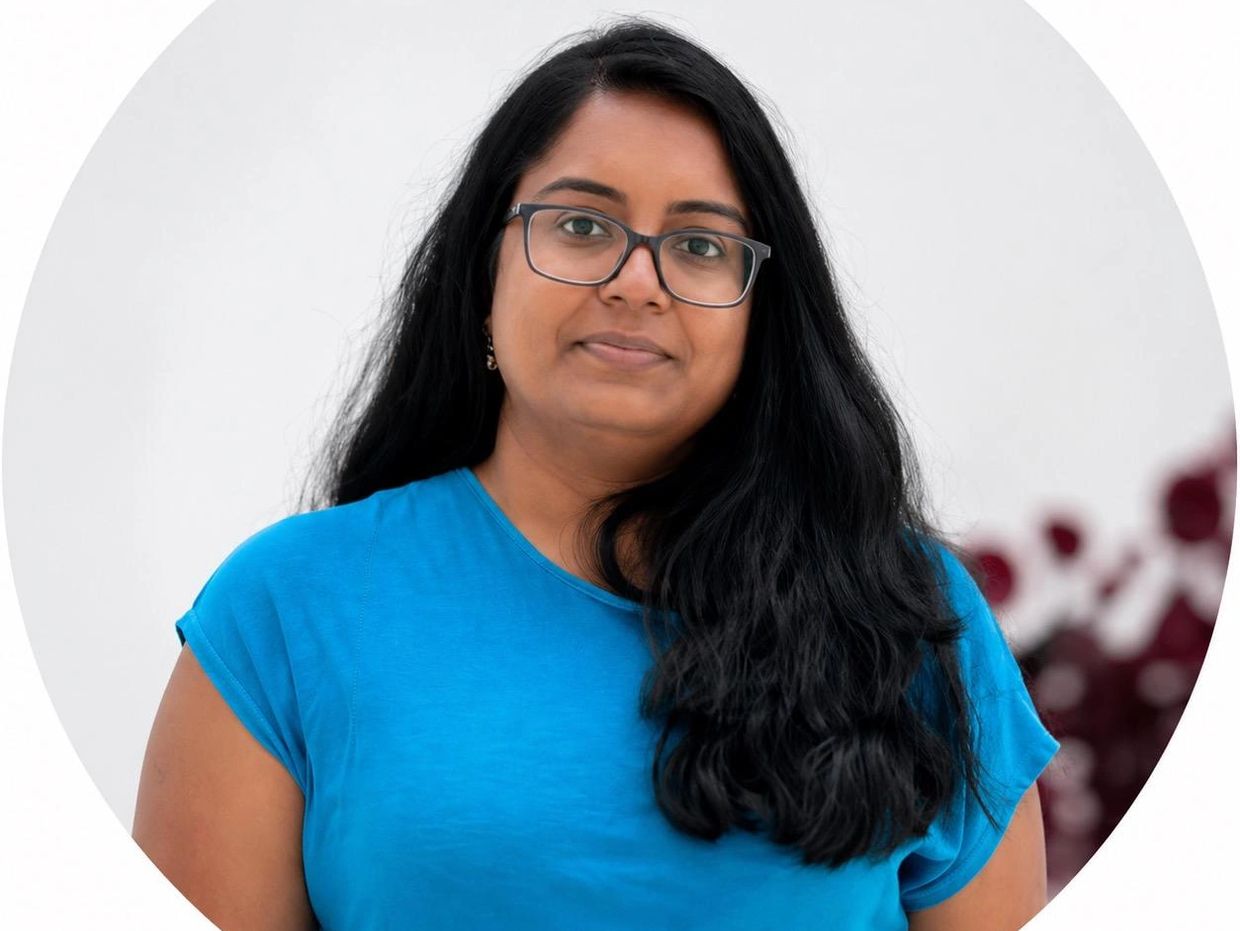 Woman with long black hair and glasses wearing a blue shirt, posing calmly.