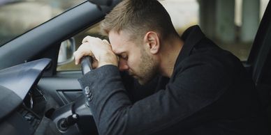 Man leaning over his steering wheel, frustrated.