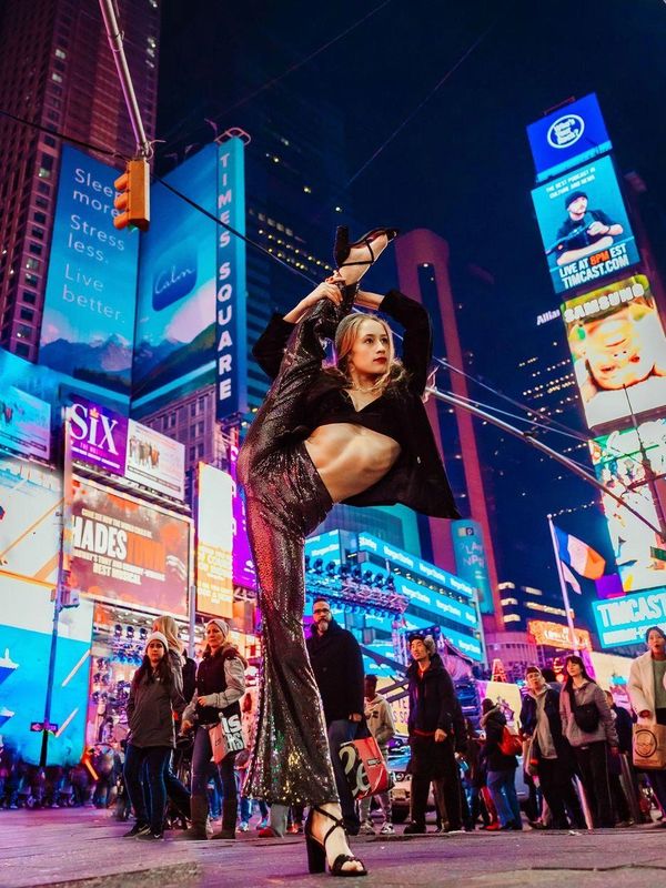 Dancer in sparkly outfit striking a high leg pose in Times Square.