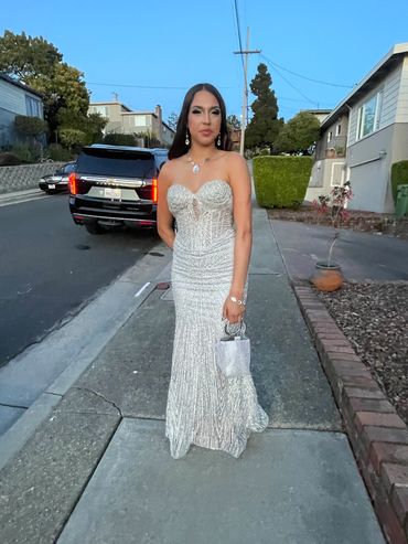 Woman in elegant white dress posing on a suburban sidewalk.