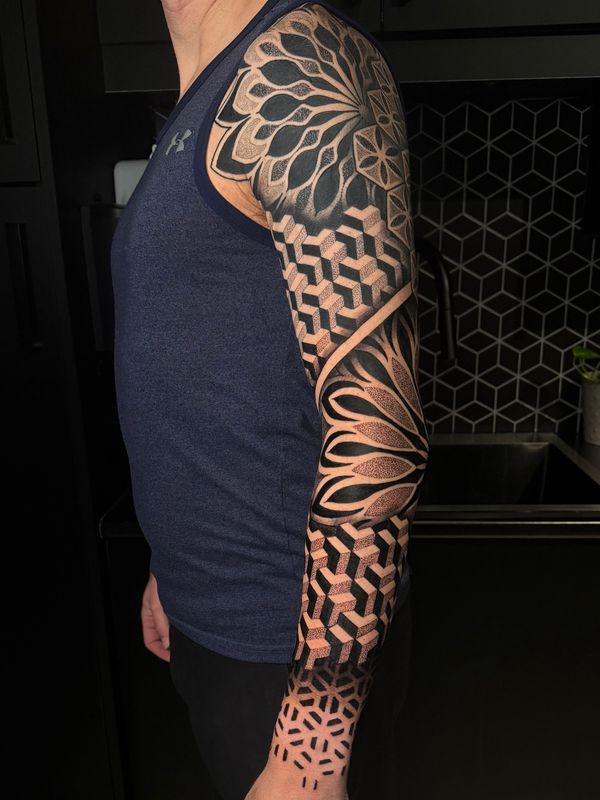 Intricate full sleeve tattoo with geometric and floral patterns in black ink.