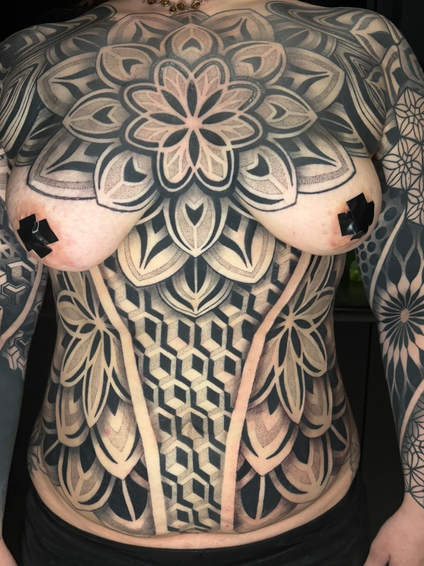 Intricate geometric and floral tattoos cover the torso and arms.