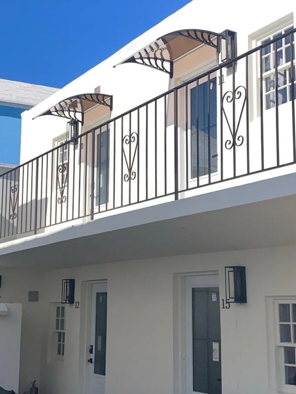 White building with doors 12 and 15 under a balcony with metal railing and awnings.