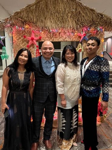 Four people dressed elegantly posing under a festive hut with colorful lights.