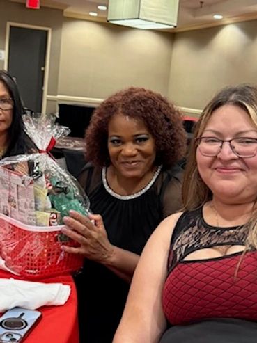 Three women sitting at a table, one holding a gift basket.