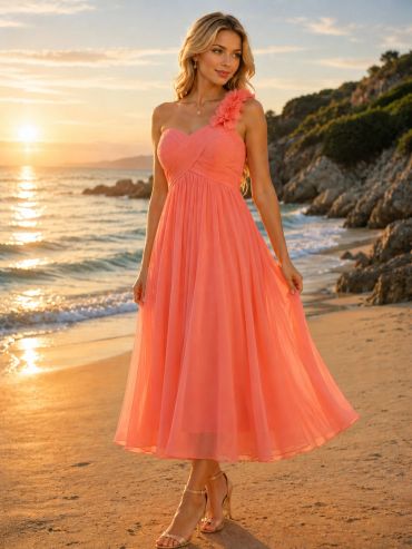 Woman in coral one-shoulder dress on the beach at sunset.