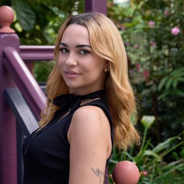 Young woman with blonde hair smiling outdoors near purple railing.