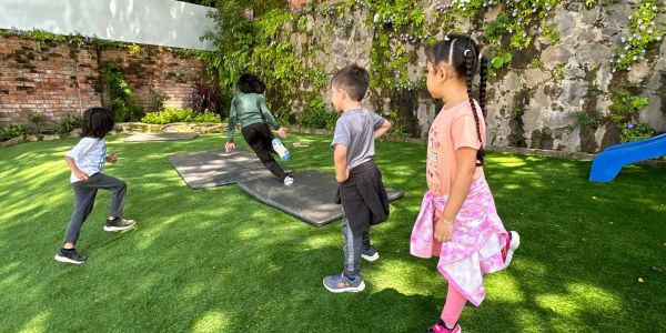 Niños jugando en jardín con piso de pasto sintético.