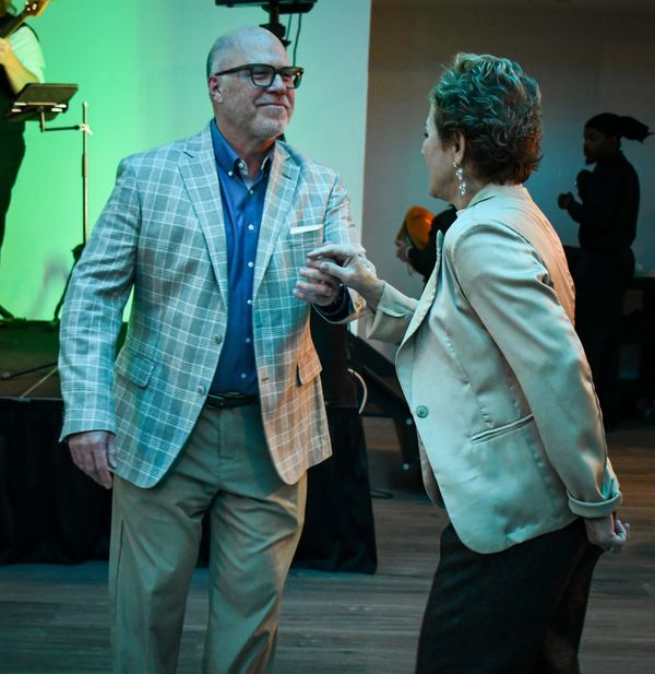 A man wearing a plaid suit jacket and woman in a gold jacket are dancing to a live band.