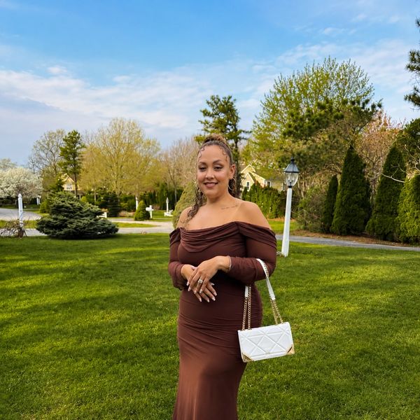 Woman in elegant brown off-shoulder dress standing on green lawn.