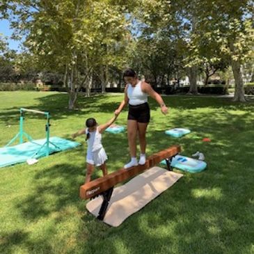 Woman helping child balance on a beam outdoors.