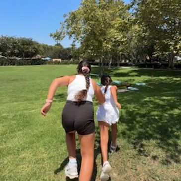 Two girls running in a park on a sunny day.