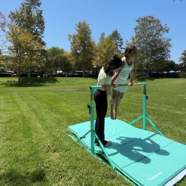 A girl practices gymnastics on a horizontal bar outdoors.