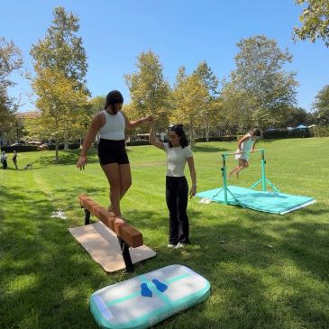 Girls practicing gymnastics outdoors on balance beam and bars.