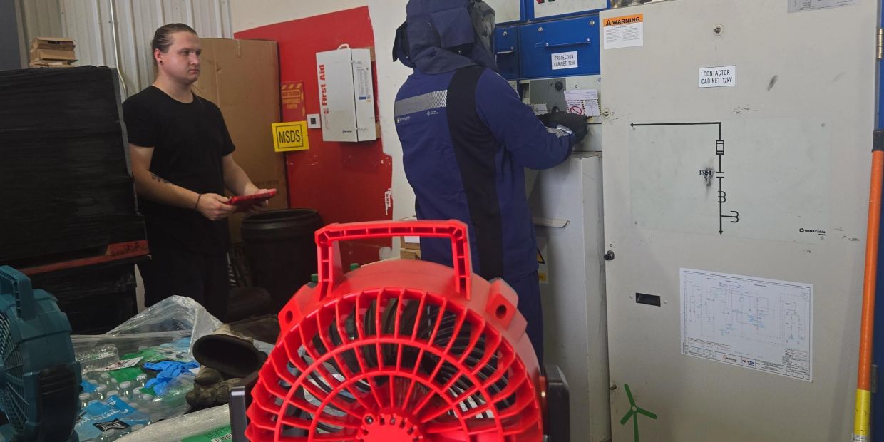 Technician working on electrical panel while another watches.