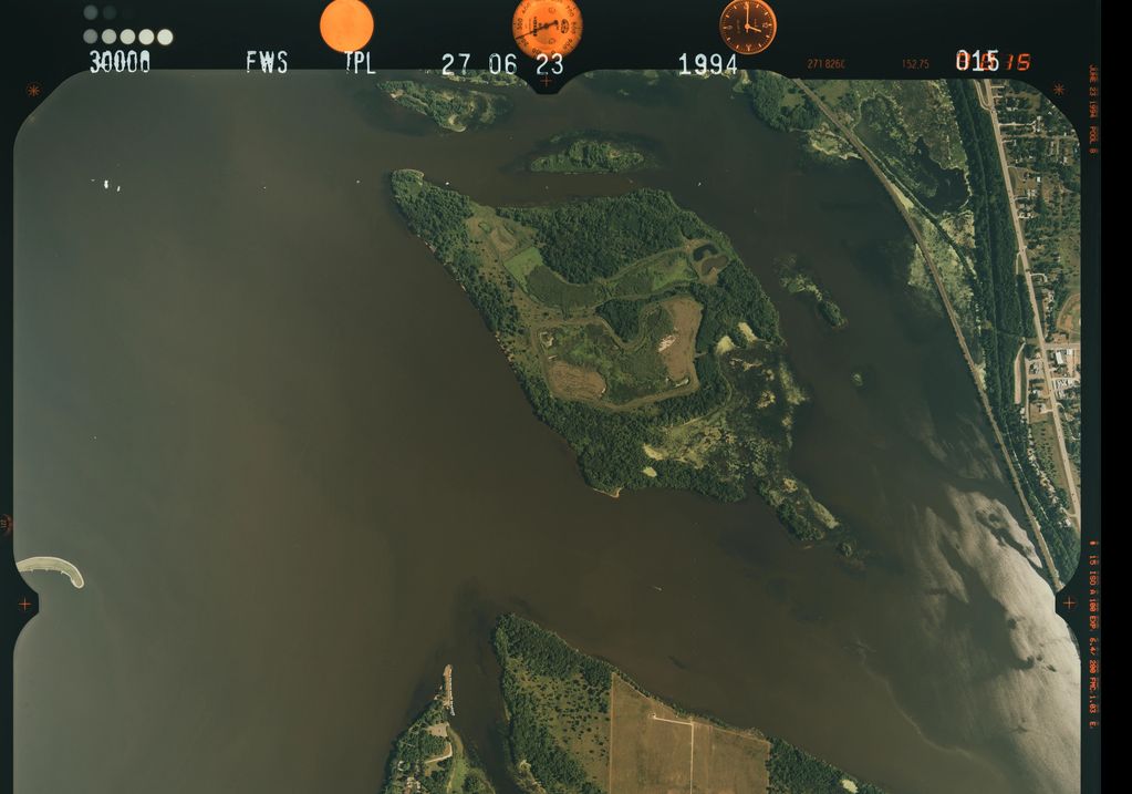 Aerial view of an island surrounded by water with green vegetation and nearby roads.
