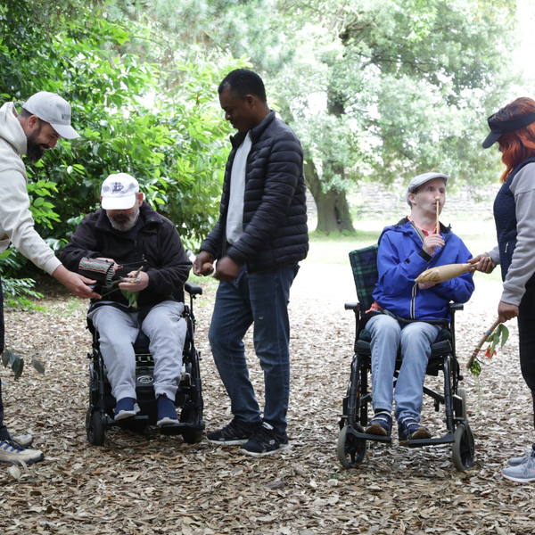 People, including two in wheelchairs, enjoy a nature walk and share plants outdoors.