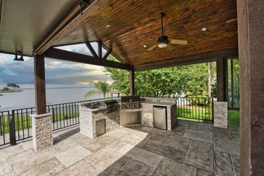 Custom covered patio with outdoor kitchen and stone flooring facing the lake in The Colony, Tx
