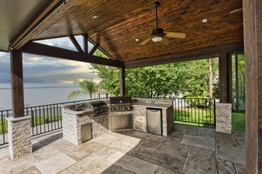 Custom covered patio with outdoor kitchen and stone flooring facing the lake in The Colony, Tx