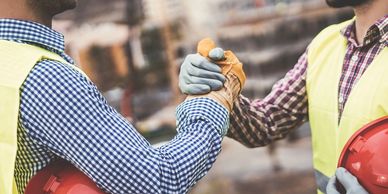 Construction workers in checkered shirts and vests, celebrating collective success with a handshake.