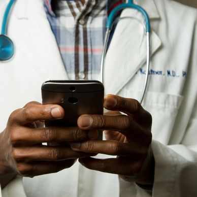 Doctor in white coat using a smartphone with a stethoscope around the neck.