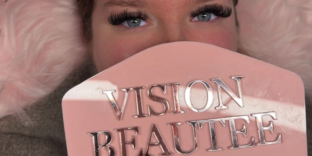 Close-up of a person with dramatic eyelashes holding a pink sign that says "VISION BEAUTE".