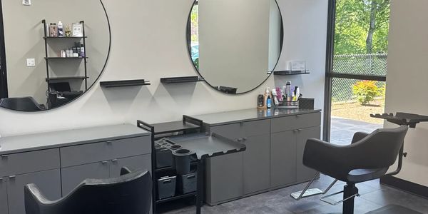Modern salon interior with black chairs and large round mirrors.