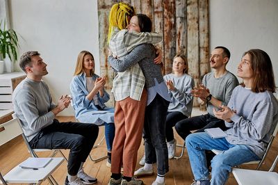 Two people embracing while others applaud in a group setting.