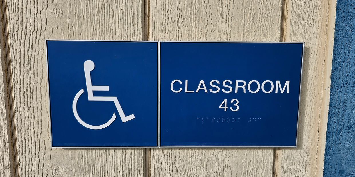 Blue & white ADA(with brail) sign with a Handicap logo that reads "Classroom 43" framed by metal.