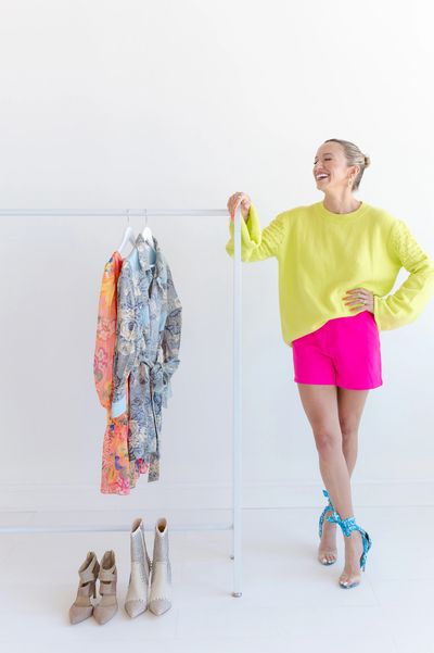 Woman in bright outfit standing next to colorful clothes and shoes on a rack.