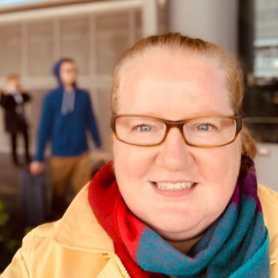 Smiling woman with glasses and colorful scarf outdoors.