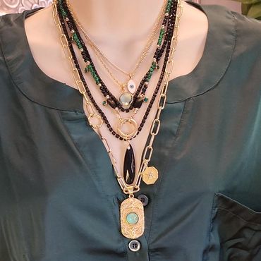 Stacked gold, black, green, and teal necklaces of arying lengths