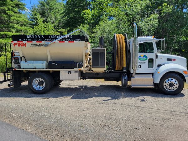 A utility truck with hose reels and equipment parked on a gravel surface.