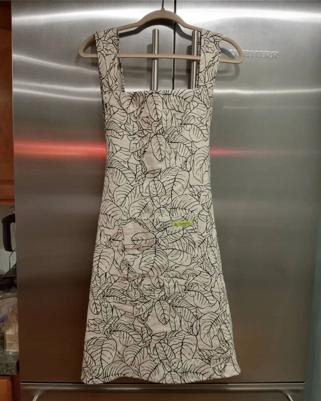 Cross back apron in linen flower print fabric hanging on the refrigerator.