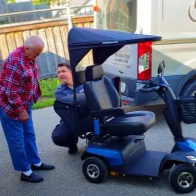 Man fixing mobility scooter with elderly person watching.