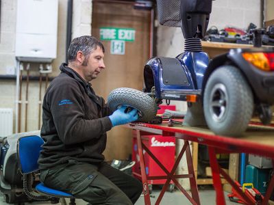 Man repairs mobility scooter tire in workshop.