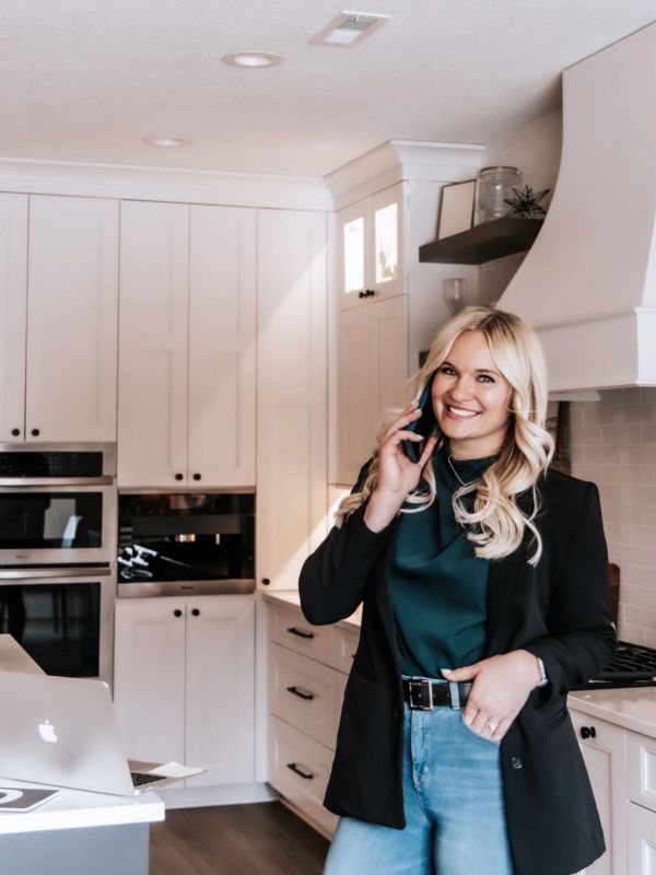 Woman talking on phone in kitchen with laptop.