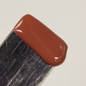 Close-up of a metal spatula with brown paint or liquid on its edge.
