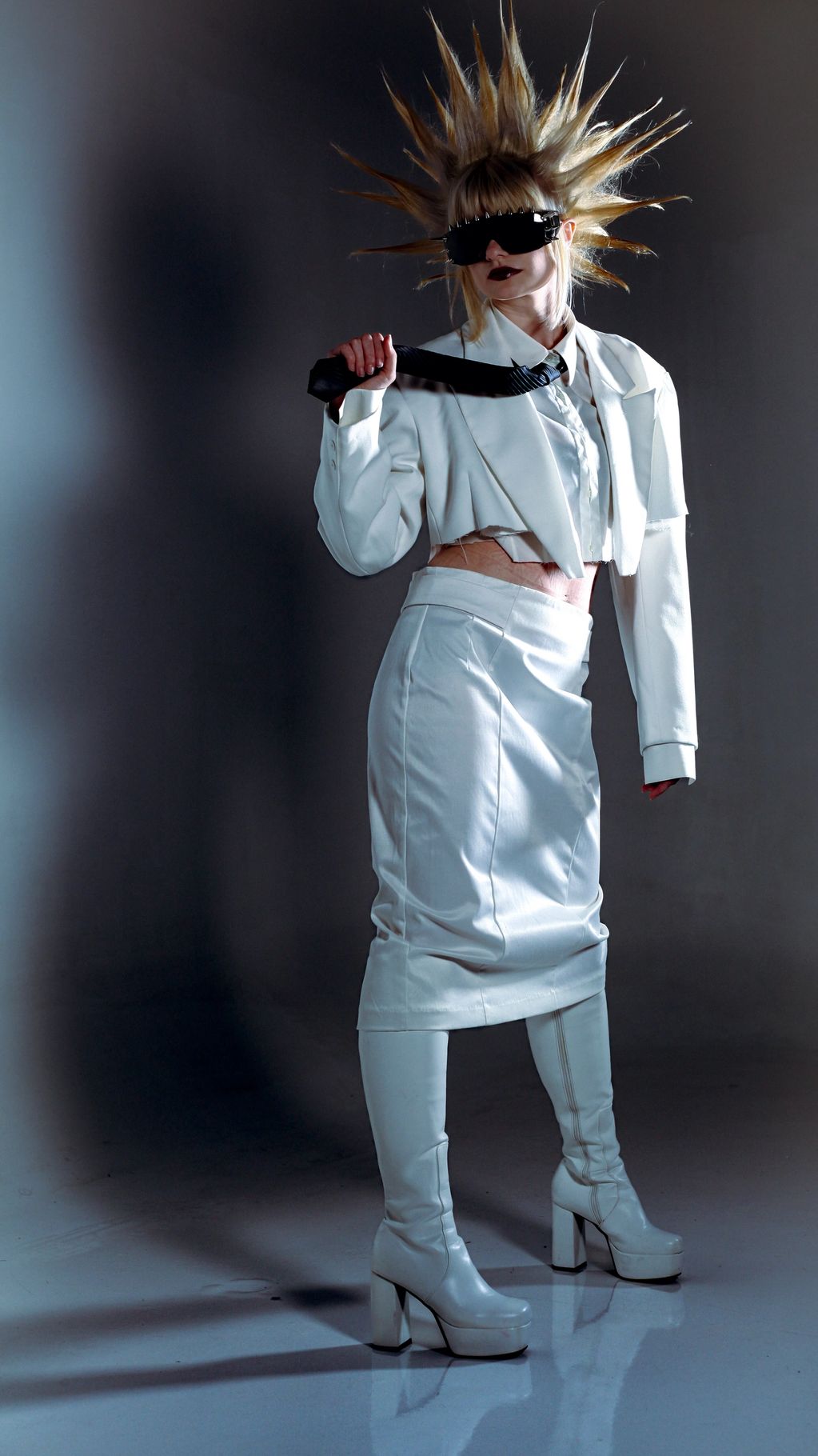 Fashion model in futuristic white outfit with spiked hair and large sunglasses.