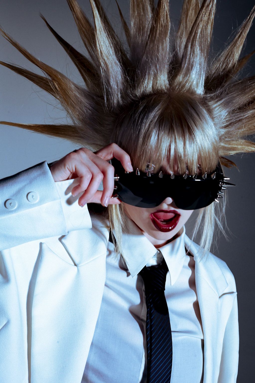 Person with spiked hair and spiked sunglasses in white outfit.
