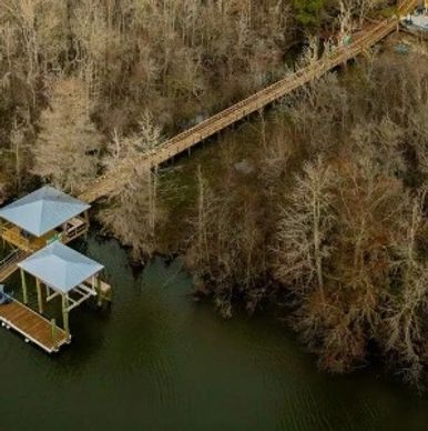 A wooden dock and walkway extending into a calm river surrounded by leafless trees.
